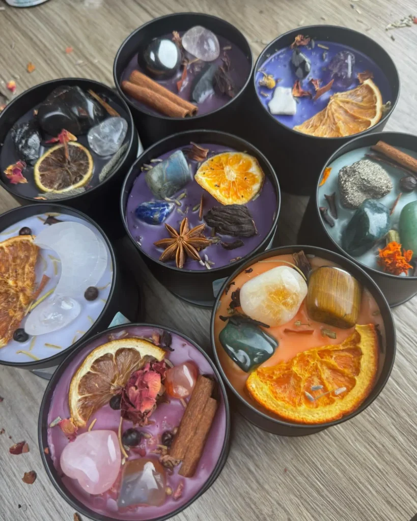 candle intentions 1 - Canvas, Corks & Forks Several round black bowls filled with colorful wax and floating dried fruits, spices, and petals (purple, pink, orange) used as scented candles or potpourri potpourri centerpieces.